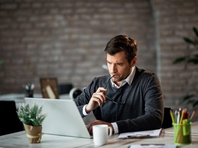 Serious businessman using laptop at work and contemplating about e-mail he has received.